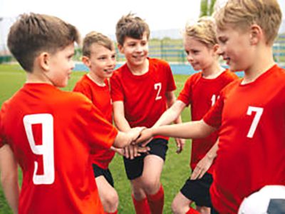 Happy boys play team sport. Kids smiling in school sports team. Junior sports teamwork; kids put hands together. Cheerful children boys players of school soccer team. Happy boys in youth football team